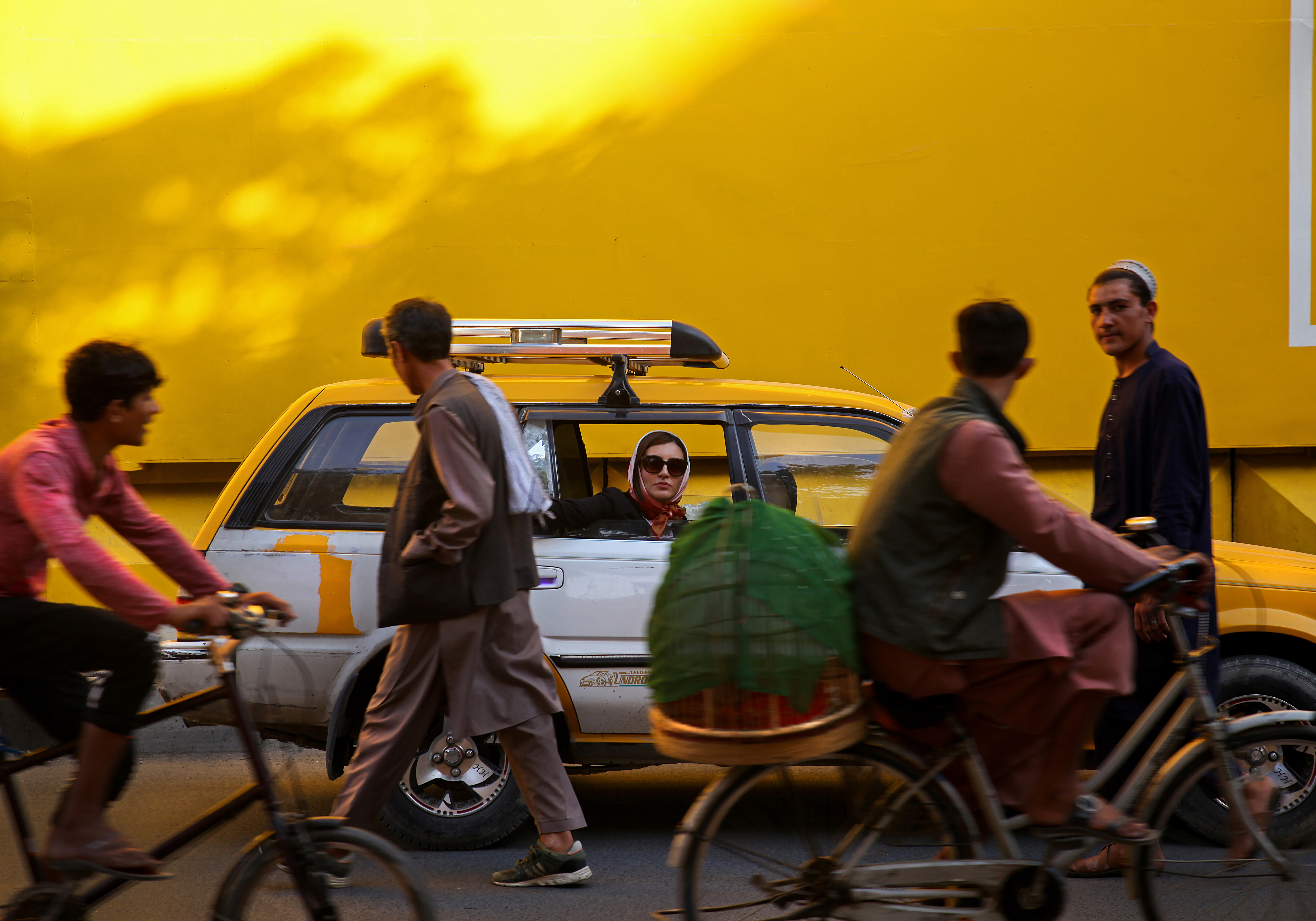 Street life in front of a sunlit yellow wall